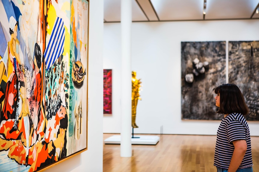 A side-on photo of a woman standing back to look at a large colourful modern artwork.