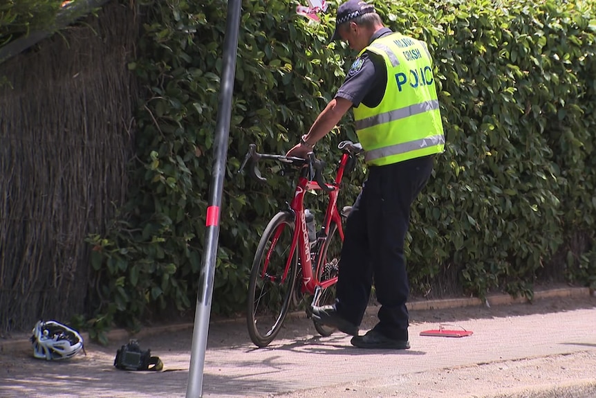 A police officer holds up a red bike with a helmet next to it