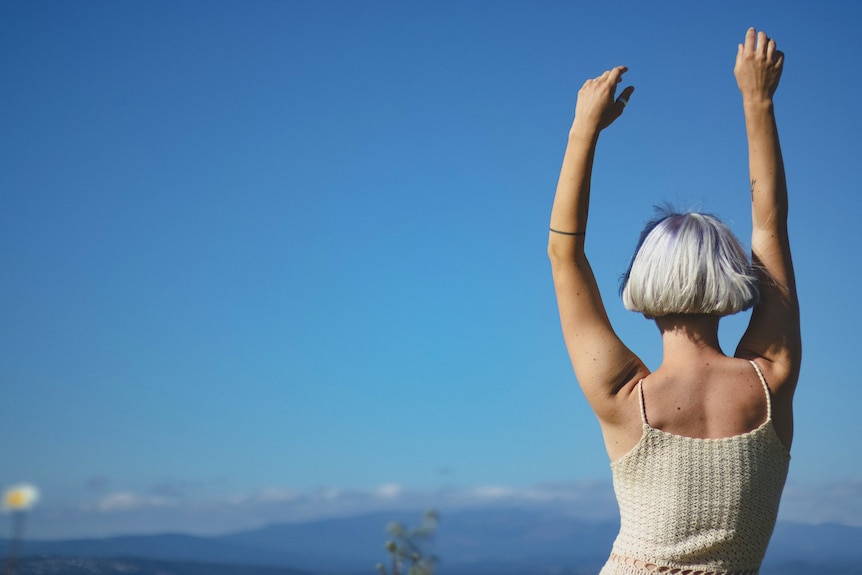 Woman with short hair overlooking the vast sky with her arms raised above her head.