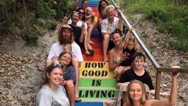 A group of people sit on rainbow-coloured steps around the slogan 'how good is living'.