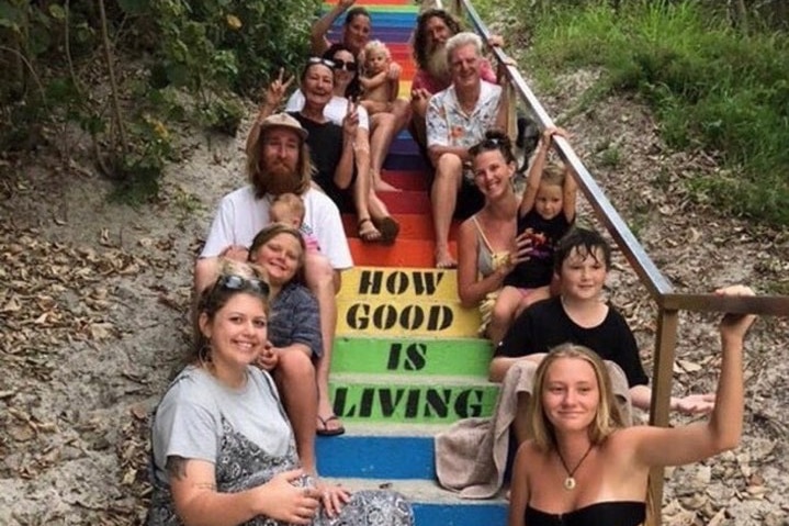 A group of people sit on rainbow-coloured steps around the slogan 'how good is living'.