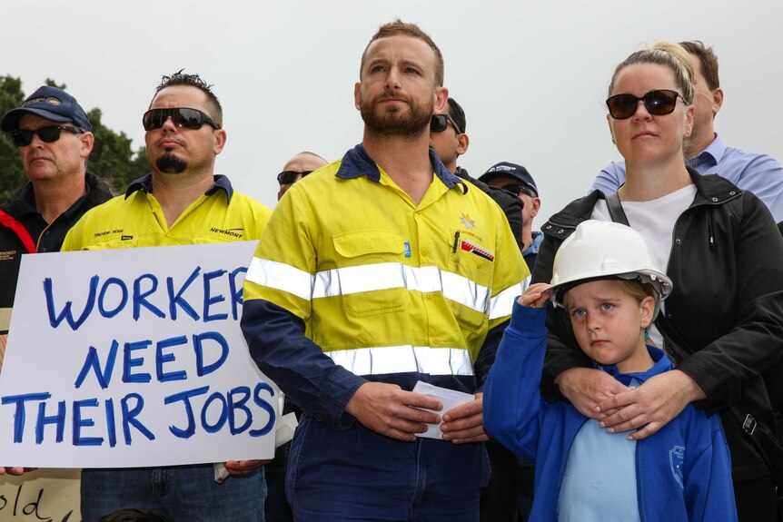 A group of people including two mine workers dressed in hi-vis gear stand alongside a boy wearing a hard hat.
