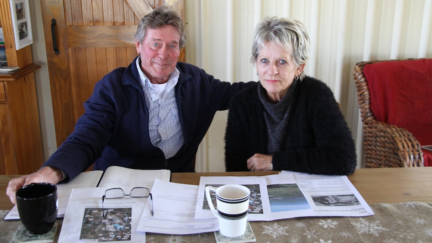 A man and a woman sit at a kitchen table, drinking tea, looking at documents. 