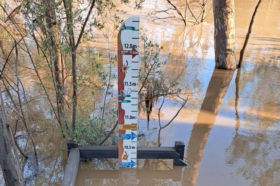 Brown water from the flooded river has almost reached the top of the railings on a set of steps which has a flood marker on it