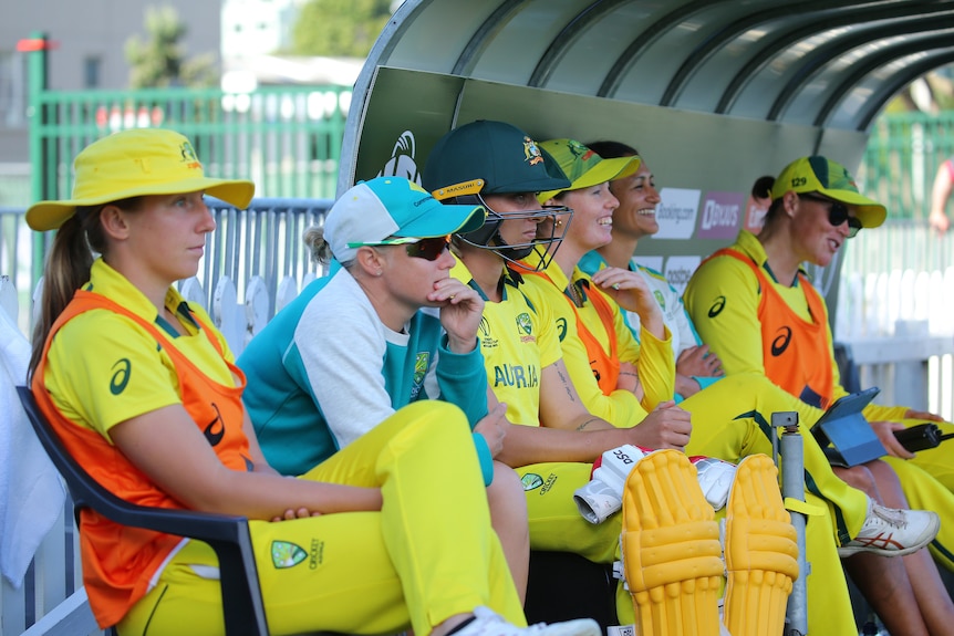Australian players sit on the bench together and watch the team play