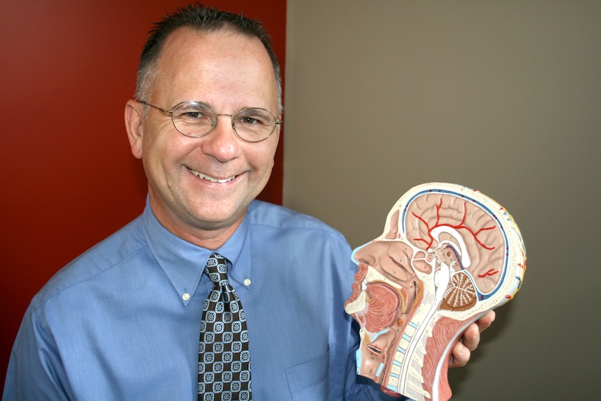 A man in a blue long-sleeved shirt with short hair holds a 3D diagram of a human head.