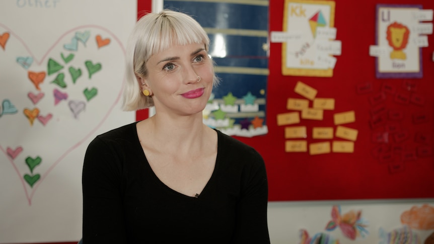 Maddy Tyers smiling in a classroom decorated with colourful drawings.