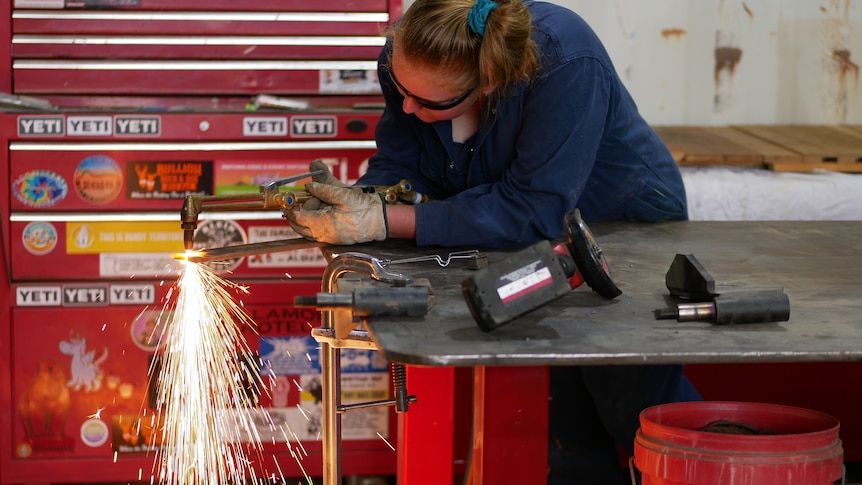A woman in overalls using a torch to cut metals