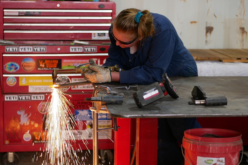 A woman in overalls using a torch to cut metals