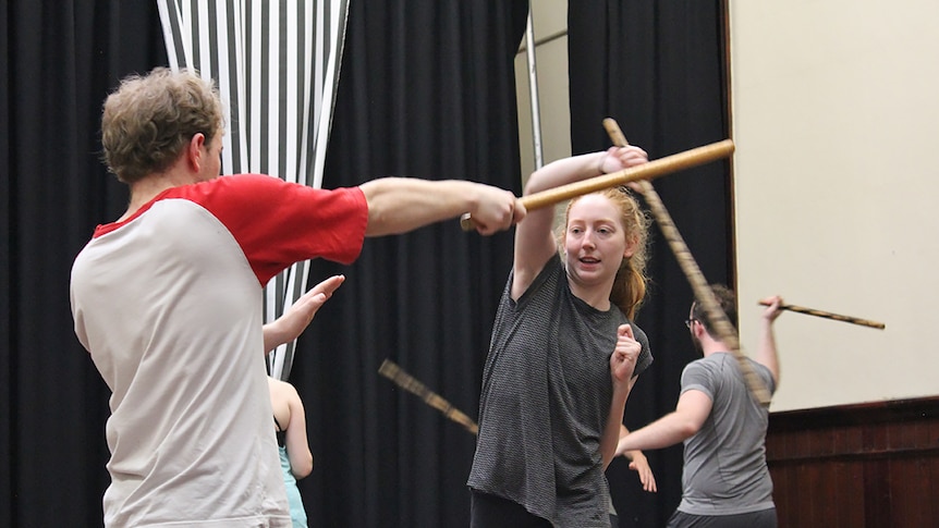 A young woman and a young man fight each other using bamboo sticks at an actors training workshop