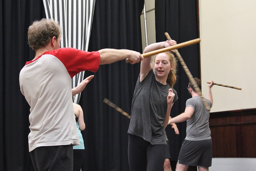 A young woman and a young man fight each other using bamboo sticks at an actors training workshop