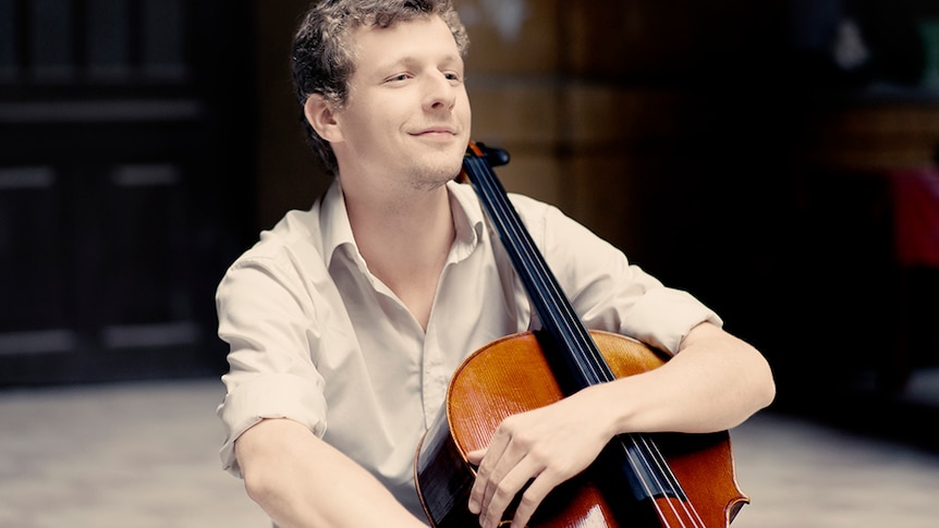 A photo of cellist István Várdai holding his cello and smiling casually.