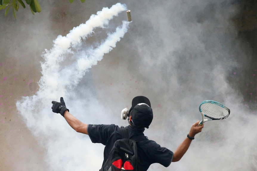 A man holds aloft a tennis racket, about to smack a smoke bomb forward 