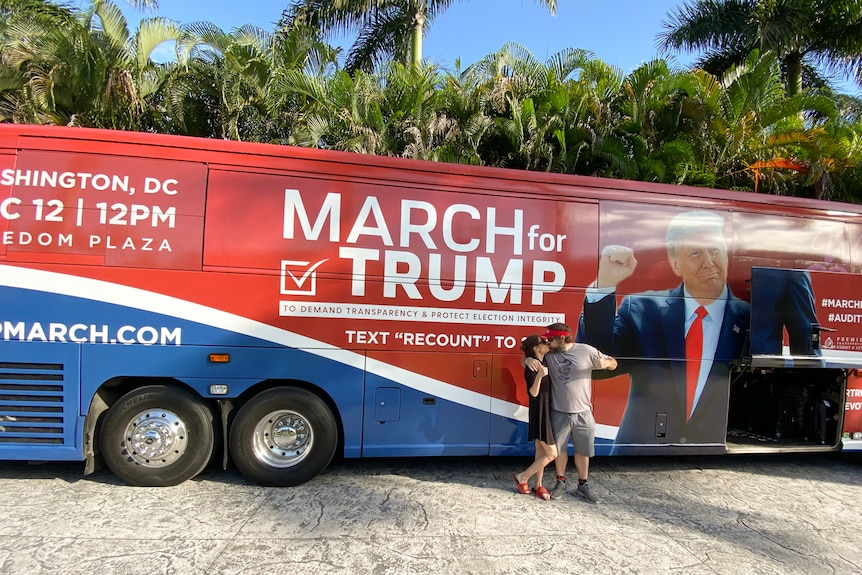 A man and a woman pose infront of a bus emblazoned with Donald Trump