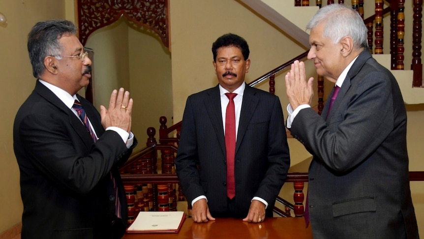 Two men greet each other with clasped hands as a third looks on