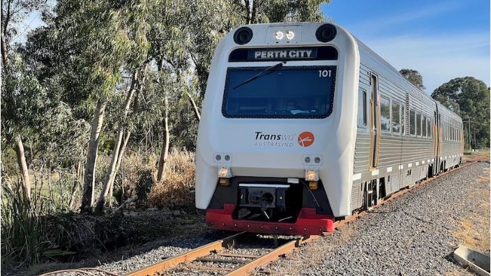 A train with Perth City on the front on a track with trees to the side