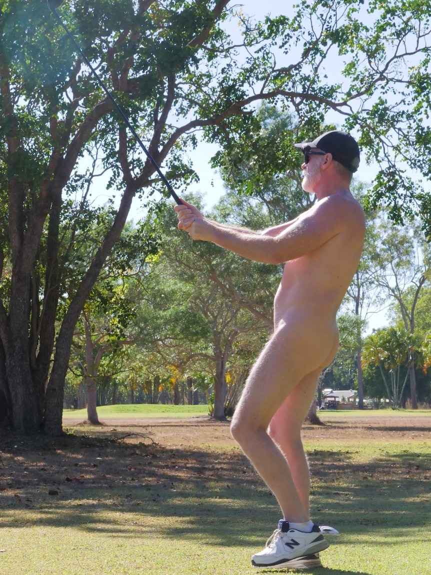 Man swinging golf club on golf green, wearing only shoes and a hat