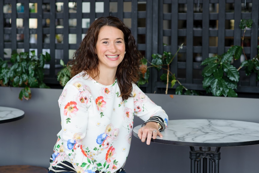 Woman wearing a white shirt with brown curly hair smiles 