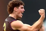 A young man with curly brown hair in an AFL top fist pumps the air.