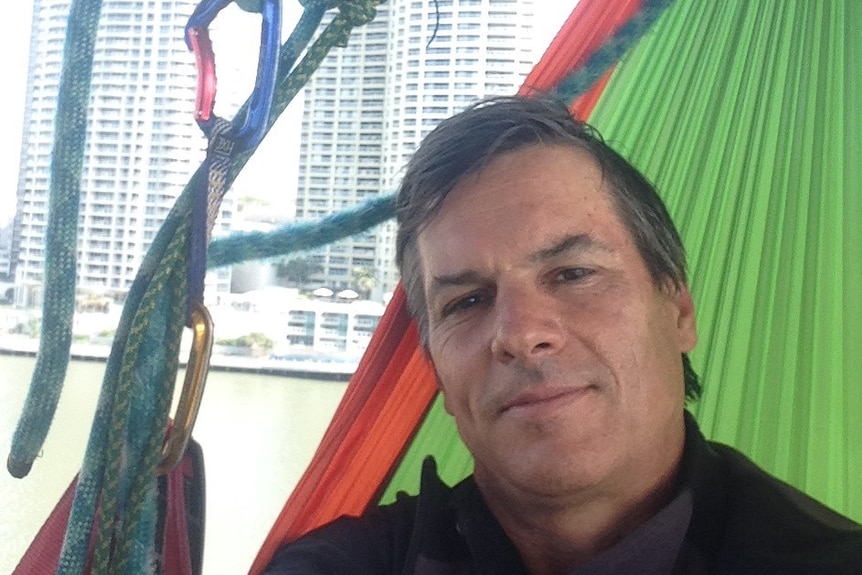 Paul Jukes looks at the camera from his hammock, with Brisbane skyscrapers in the background.