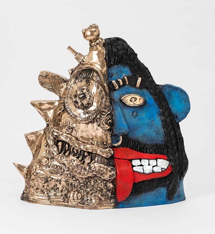 A sculptural work of a head, half cast in gold, half in blue dye, with tongue sticking out.