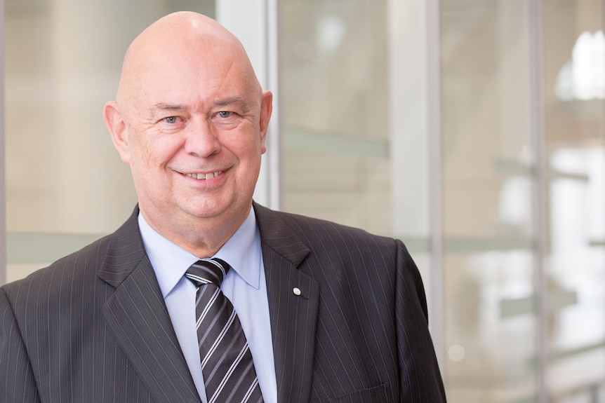 A bald man in a suit smiles at the camera