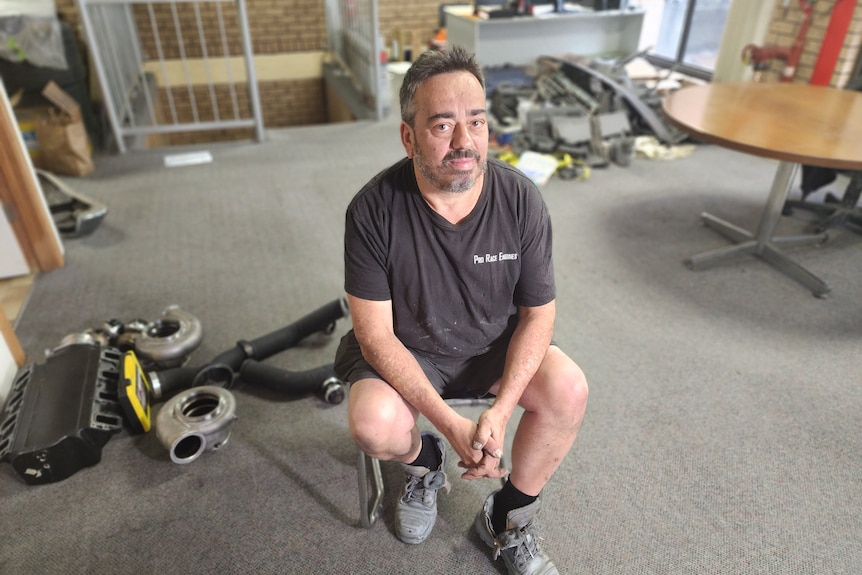 a man sits in an office with truck pieces on the floor 