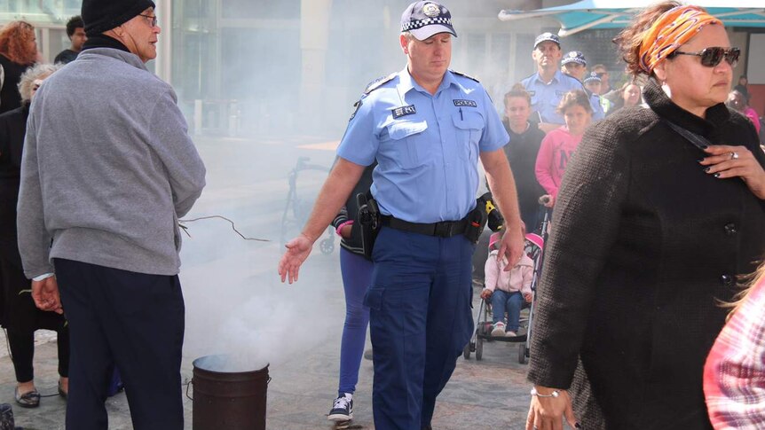 A police officer walks through smoke and past a burning can as part of a ceremony in Perth's Forrest Chase.