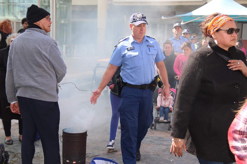 A police officer walks through smoke and past a burning can as part of a ceremony in Perth's Forrest Chase.