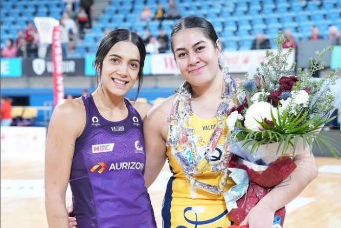 Two players stand close together. The one on the right holds a bunch of flowers and wears necklaces made out of chocolates