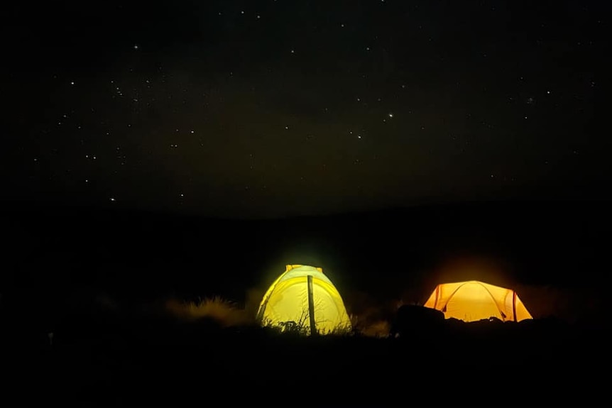 two glowing tents seen against a black sky with stars
