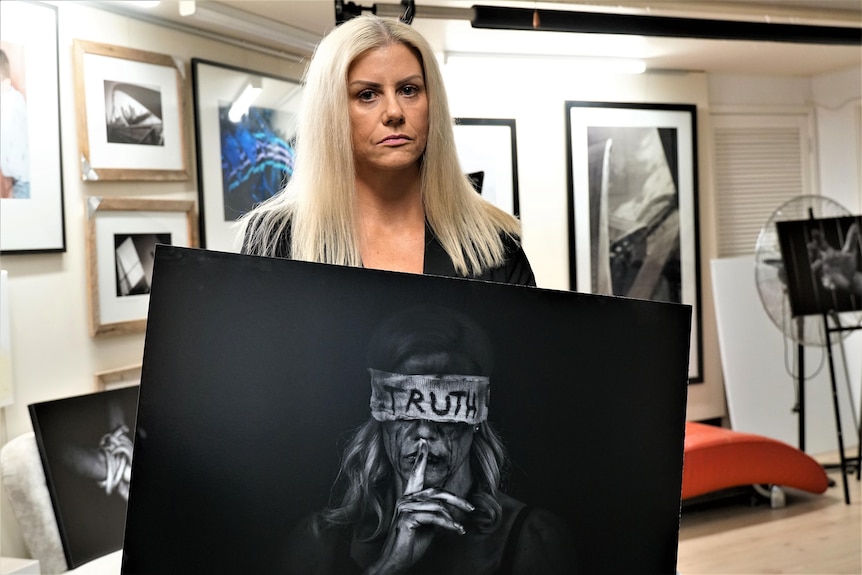 A woman with blonde hair holding a black and white dark photograph of herself