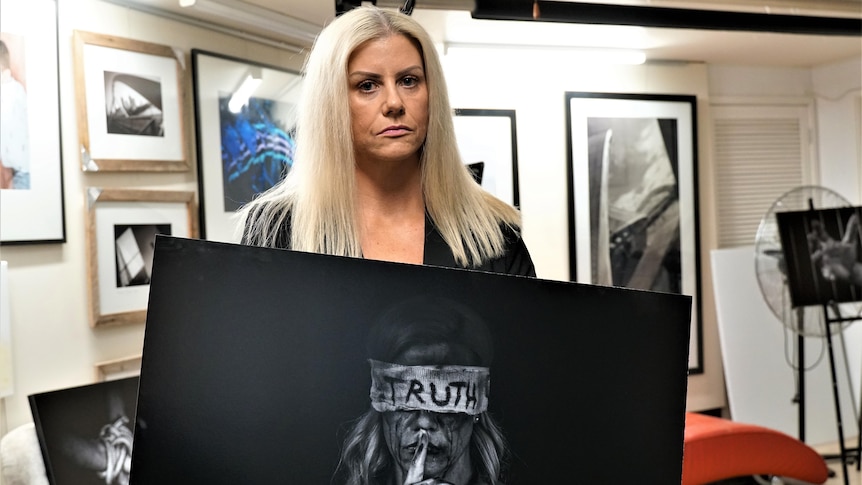 A woman with blonde hair holding a black and white dark photograph of herself