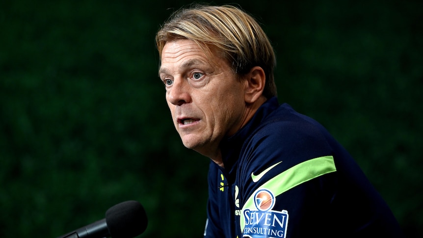 A man wearing a blue and green jumper talks into a microphone