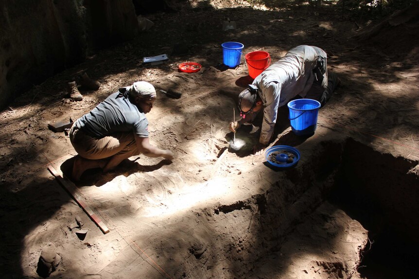 Two people carefully unearthing artefacts from the floor of the Panga ya Saidi cave in Kenya