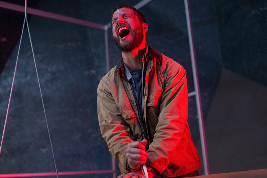 Still image of actor Logan Marshall-Green in pain whilst holding a knife to to his own hand in 2018 film Upgrade.