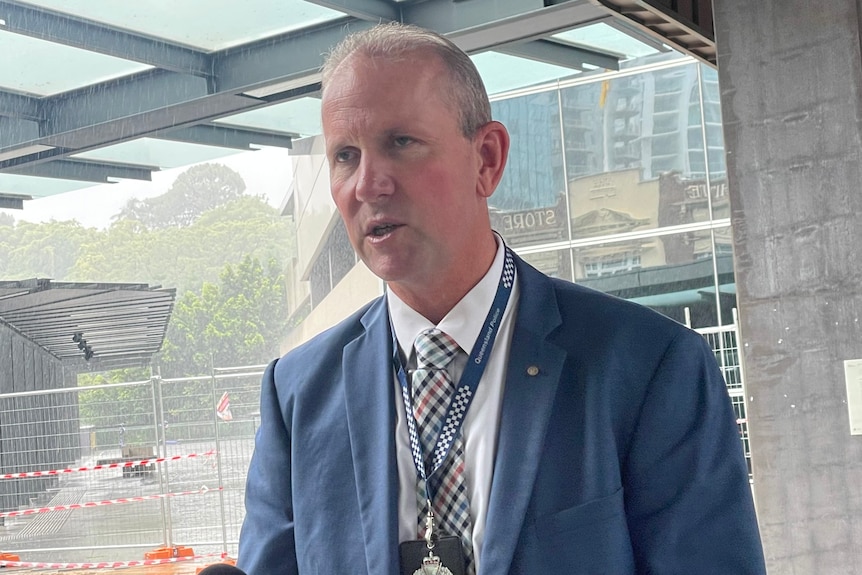 A man in a grey suit speaks to reporters.