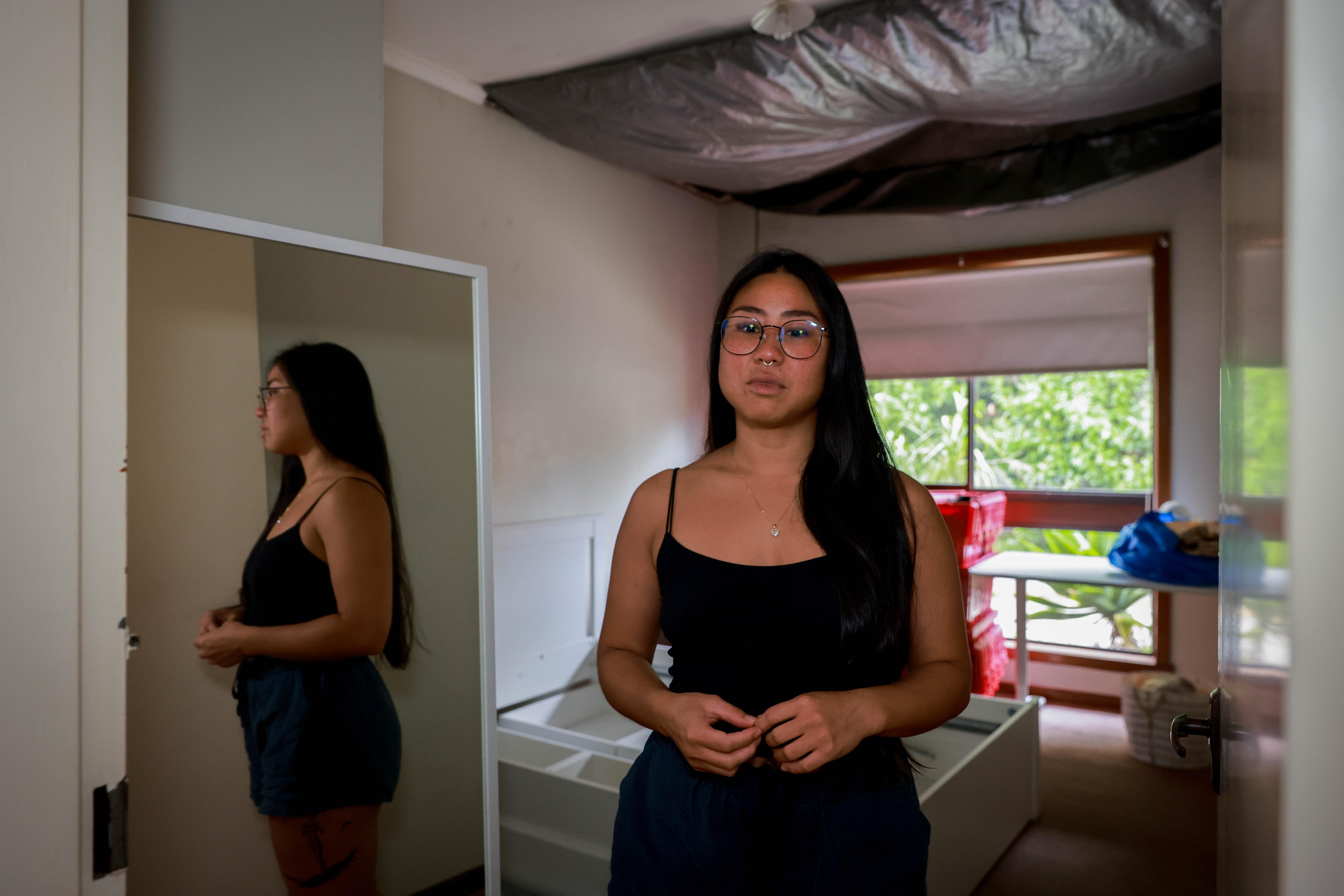 Dyxi standing in front of a bedroom with a tarp covering a chunk of missing ceiling.