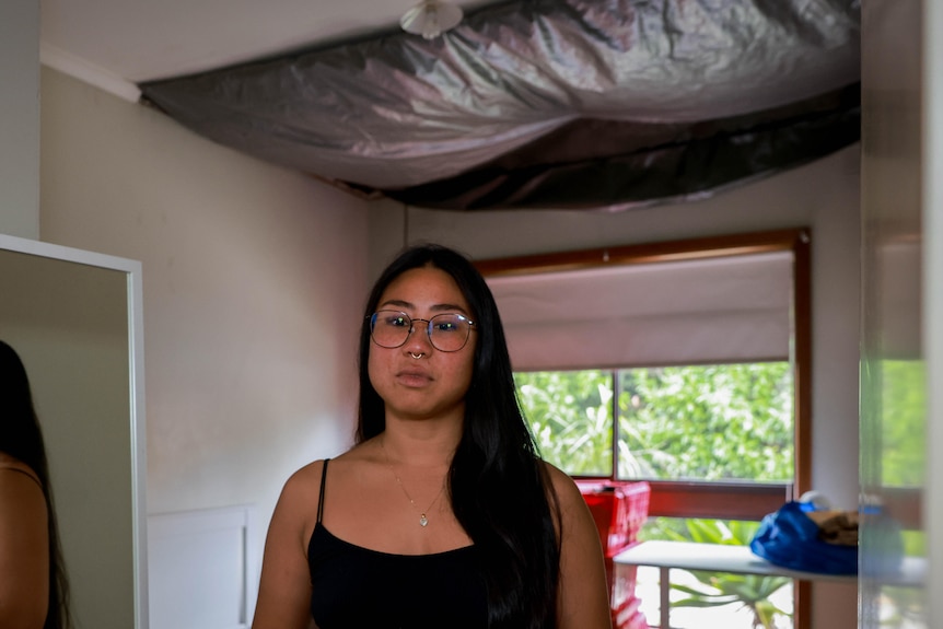 Dyxi standing in front of a room with a tarp draped over the missing chunk of ceiling.