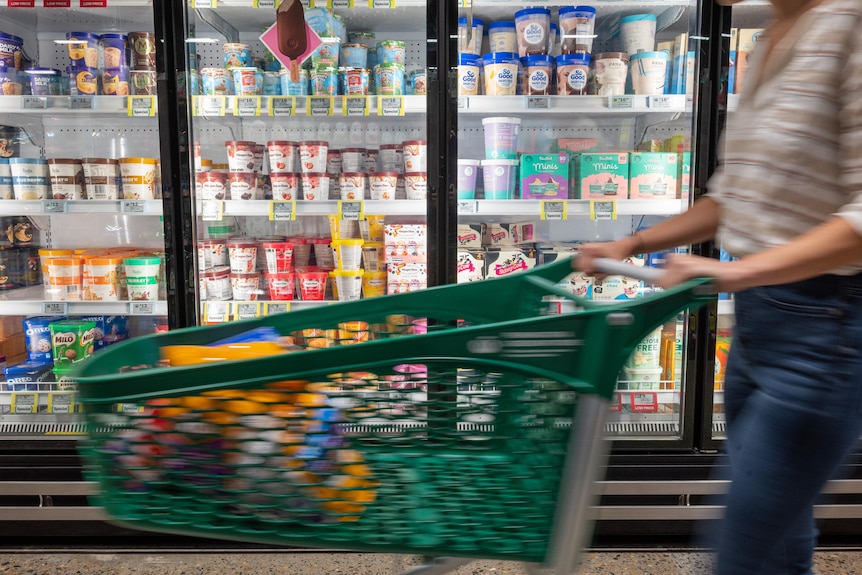 A customer wheels a trolley past an aisle of a supermarket with ice cream in freezers.