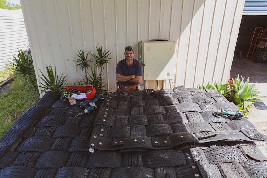 A table covered with woven tyre mats and a man standing behind them.