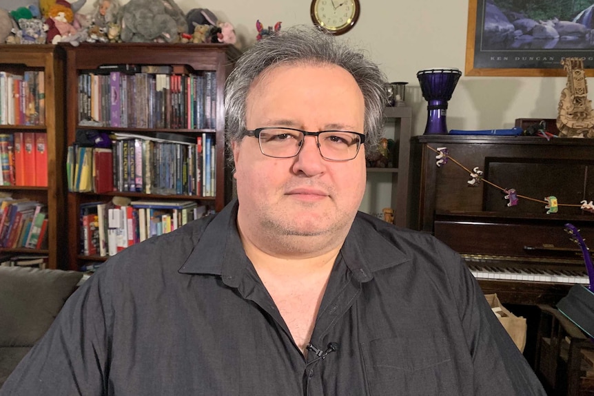 James Dominguez sitting in his lounge room in front of a shelf of books.