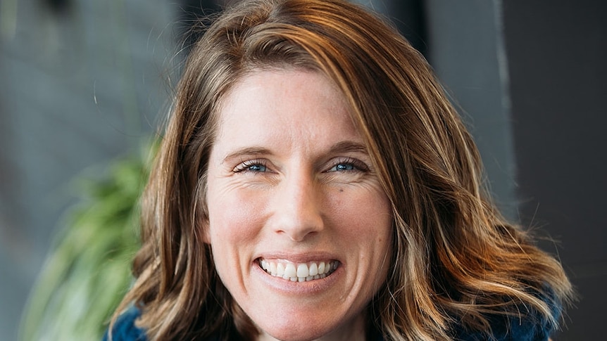 A woman with brown hair smiles at the camera, she wears a knitted snood.