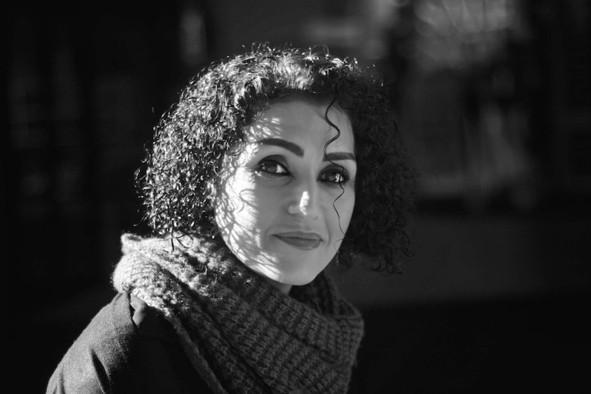 A woman with short curly hair looks towards the camera with a thoughtful expression.