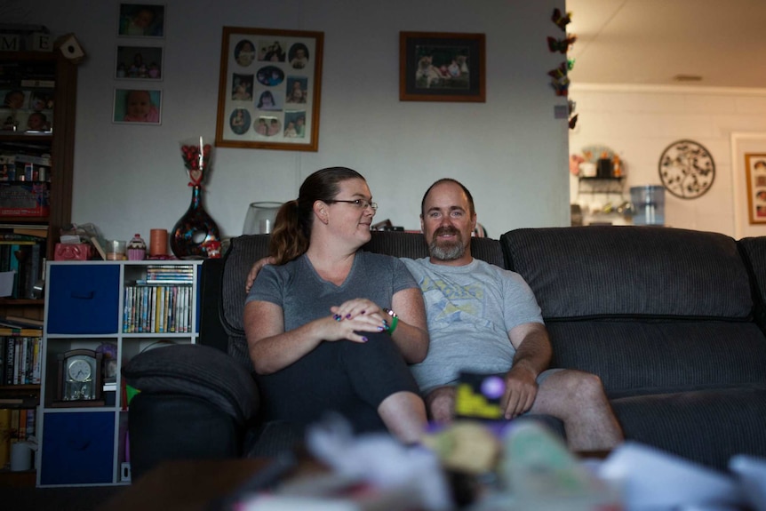 Middle aged couple sit affectionately together on a lounge in their lounge room.