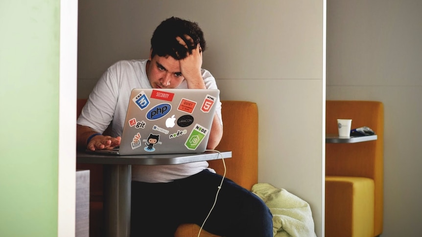 Man with hand on head at work on computer looking frustrated for story on how to get out of a job you don't like