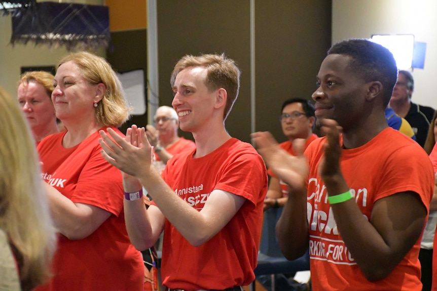 People in red shirts smile and clap.