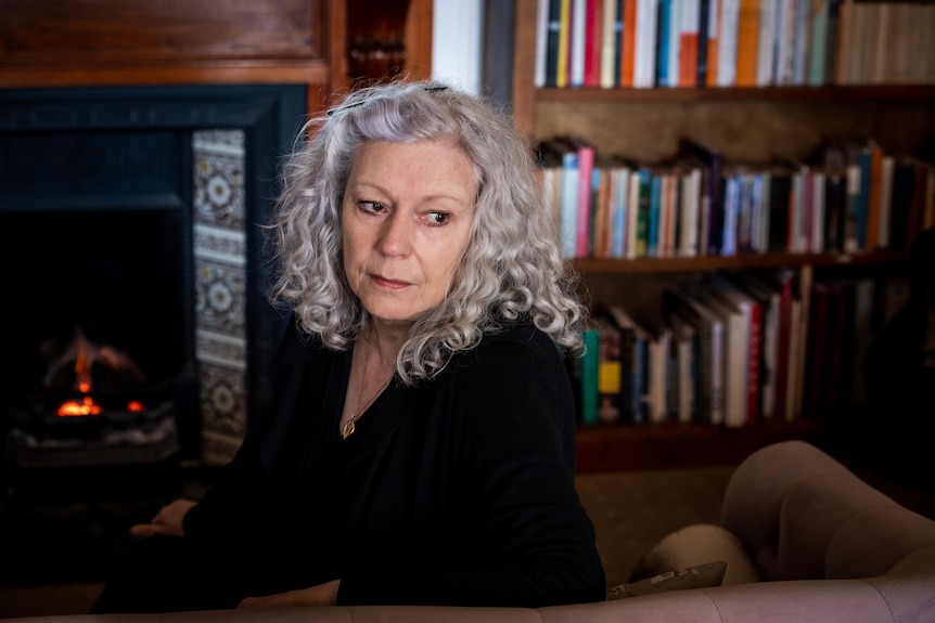 A white woman in her 70s with curly grey hair looks pensively into the camera.