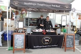 A man and a woman stand at a stall selling grass fed beef.