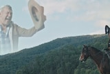 An apparition of Jimmy Barnes dressed as a cowboy in the sky above a mountain range. Kirin J Callinan looks at it atop a horse.